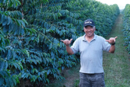 JN Coffee Farms man standing between rows of coffee trees smiling